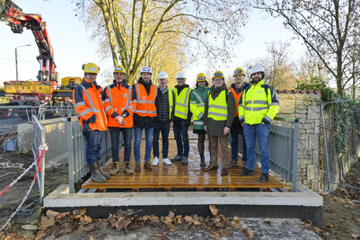 Élus et techniciens en tenue de chantier posant sur la passerelle métallique nouvellement installée