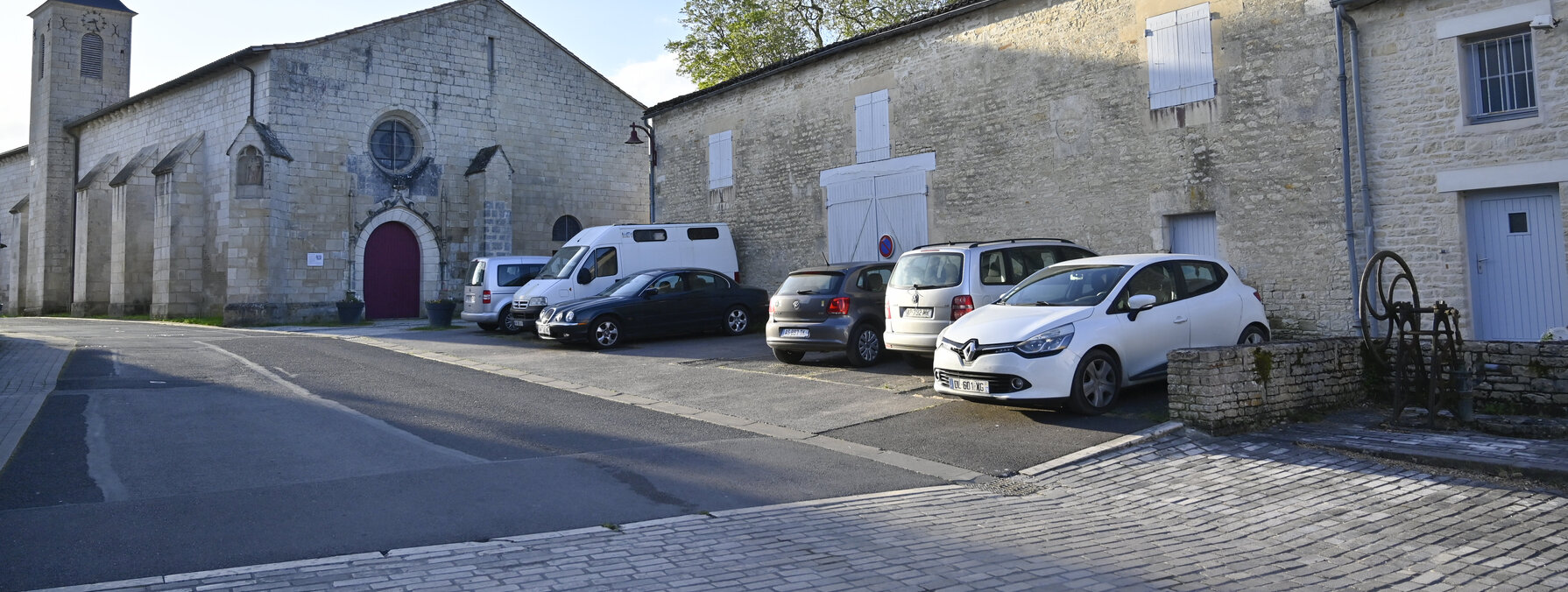 Parvis pavé devant une église en pierre de taille avec clocher et bâtiments anciens environnants