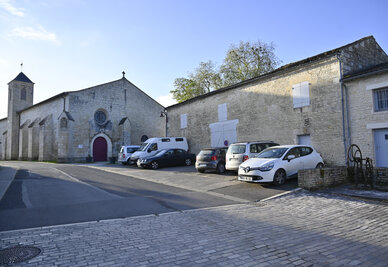 Parvis pavé devant une église en pierre de taille avec clocher et bâtiments anciens environnants