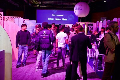 Foule de visiteurs et d'exposants circulant dans les allées animées du salon INNN, sous un éclairage violet