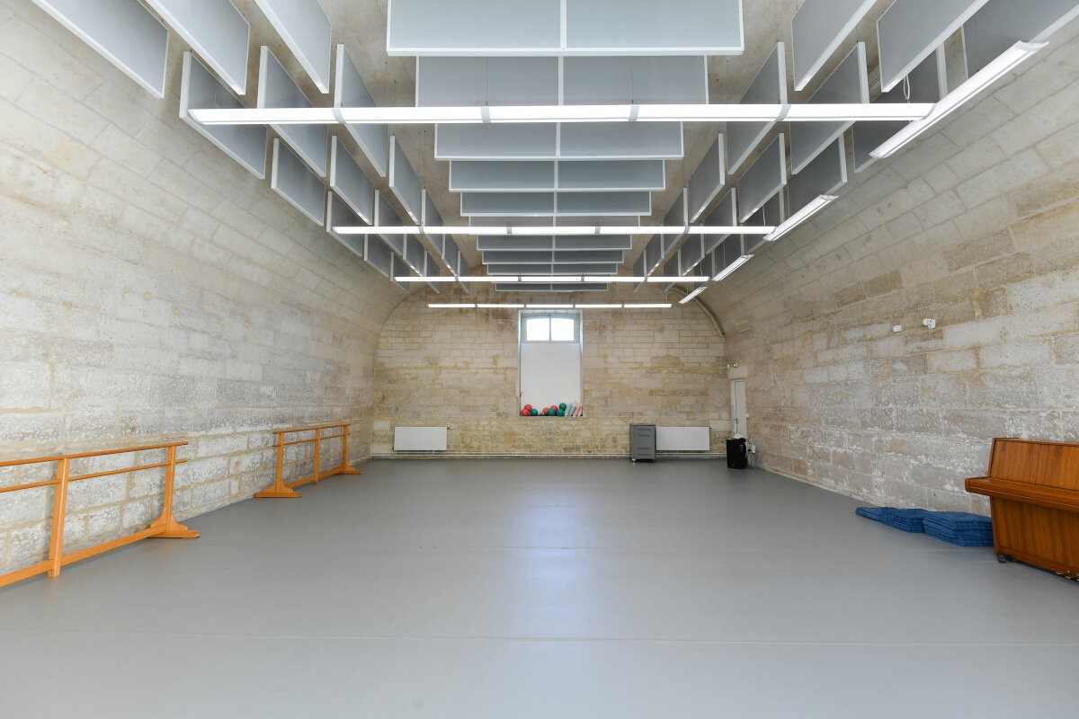 Salle de danse du Conservatoire avec barres en bois, sol en vinyle gris et plafond acoustique modulaire
