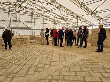 Participants sur le dallage en pierre restauré, sous la tente de chantier protégeant la terrasse du Donjon