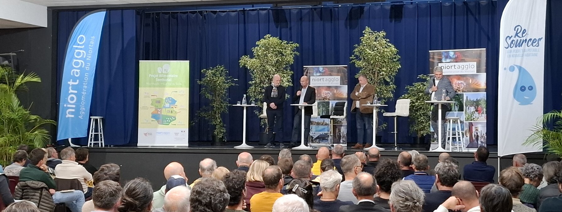 Quatre intervenants sur scène devant un large public réuni en salle pour une conférence de Niort Agglo