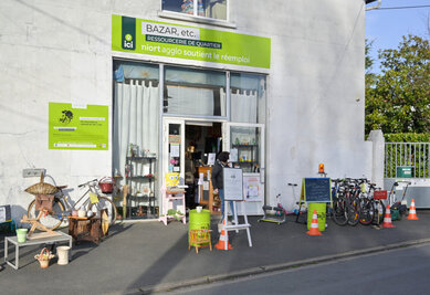 Façade de la ressourcerie Bazar, etc. avec meubles, vélos et objets de seconde main exposés devant l'entrée