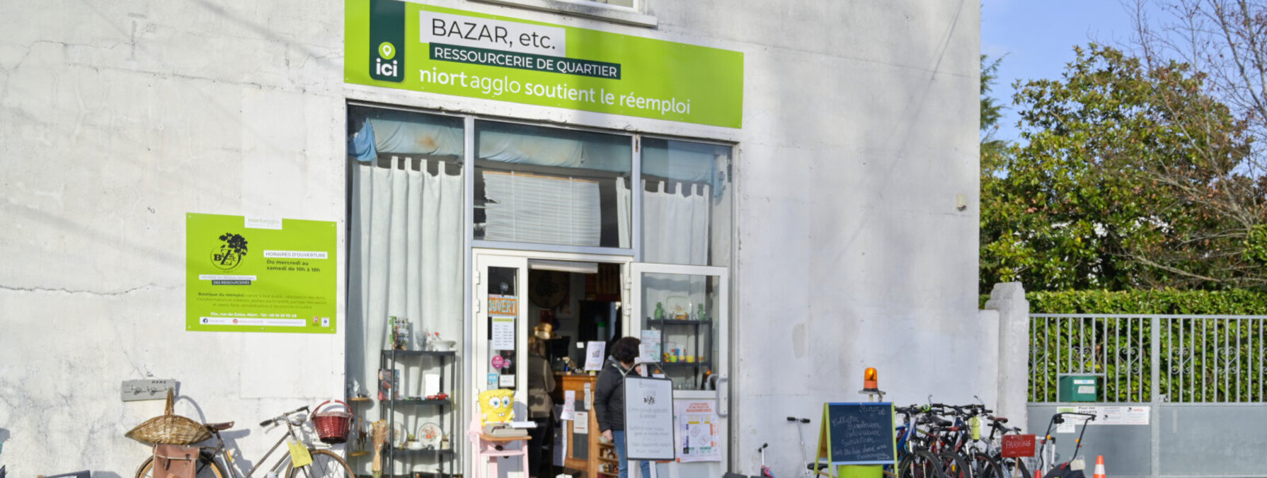 Façade de la ressourcerie Bazar, etc. avec meubles, vélos et objets de seconde main exposés devant l'entrée