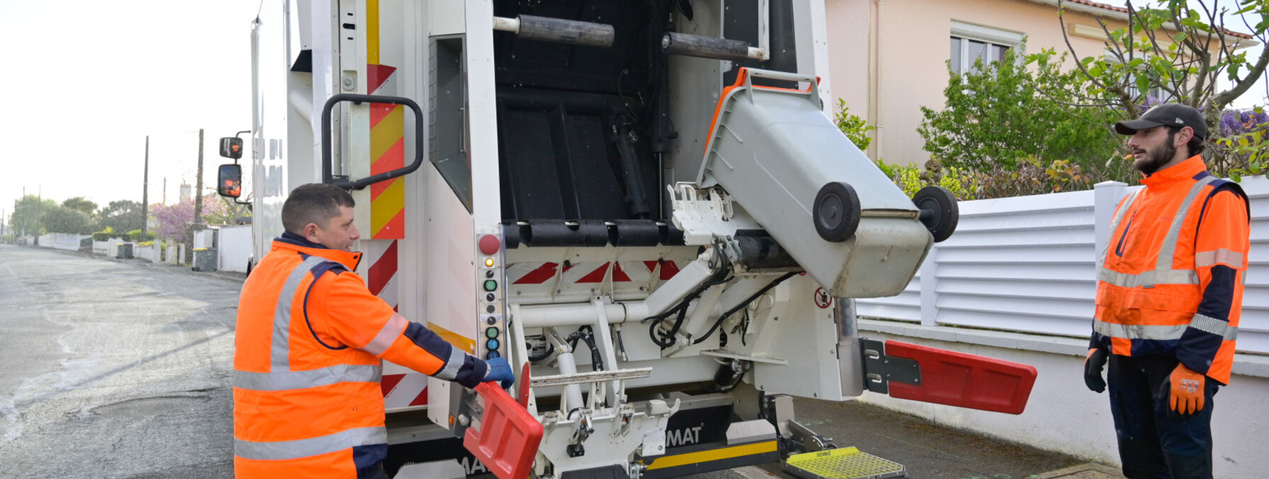 Deux ripeurs en tenue de sécurité manœuvrant la benne d'un camion de collecte des ordures ménagères en zone résidentielle