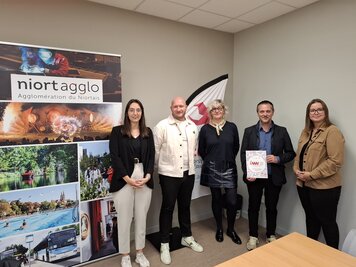 Cinq participants posant devant le roll-up Niort Agglo, l'un d'eux tenant le programme du salon, lors de la conférence de presse.