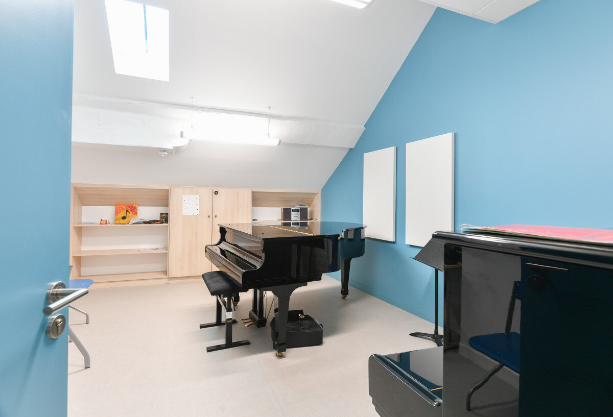Salle de cours du Conservatoire avec piano à queue noir, pupitre, étagères en bois et panneaux acoustiques muraux