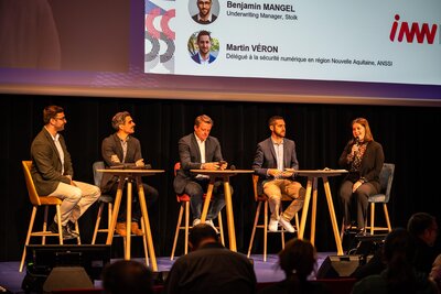 Cinq intervenants en table ronde sur la scène du salon INNN, dont les noms sont projetés sur grand écran