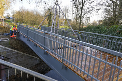 Passerelle suspendue par des chaînes de grue au-dessus de la Romagne, deux ouvriers en équipements de sécurité à l'ouvrage