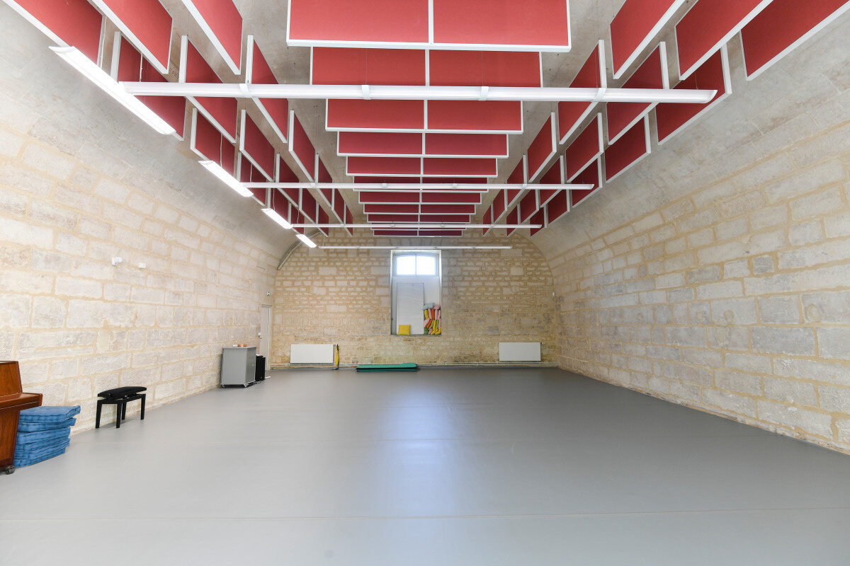 Salle de répétition aux murs en pierre de taille, sol souple gris et plafond acoustique à panneaux rouges