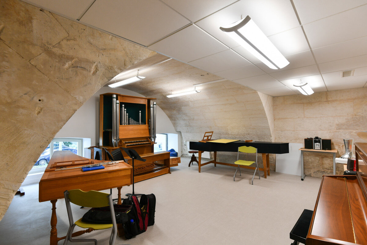 Salle de pratique musicale voûtée en pierre avec orgue de chambre, clavecin et pupitres