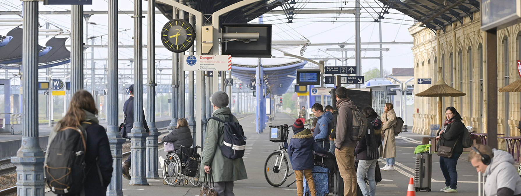 Quai de la gare de Niort avec des voyageurs dont une personne en fauteuil roulant, sous la marquise