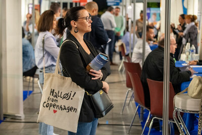 Participante consultant un programme du salon, avec des entretiens entre candidats et recruteurs en arrière-plan