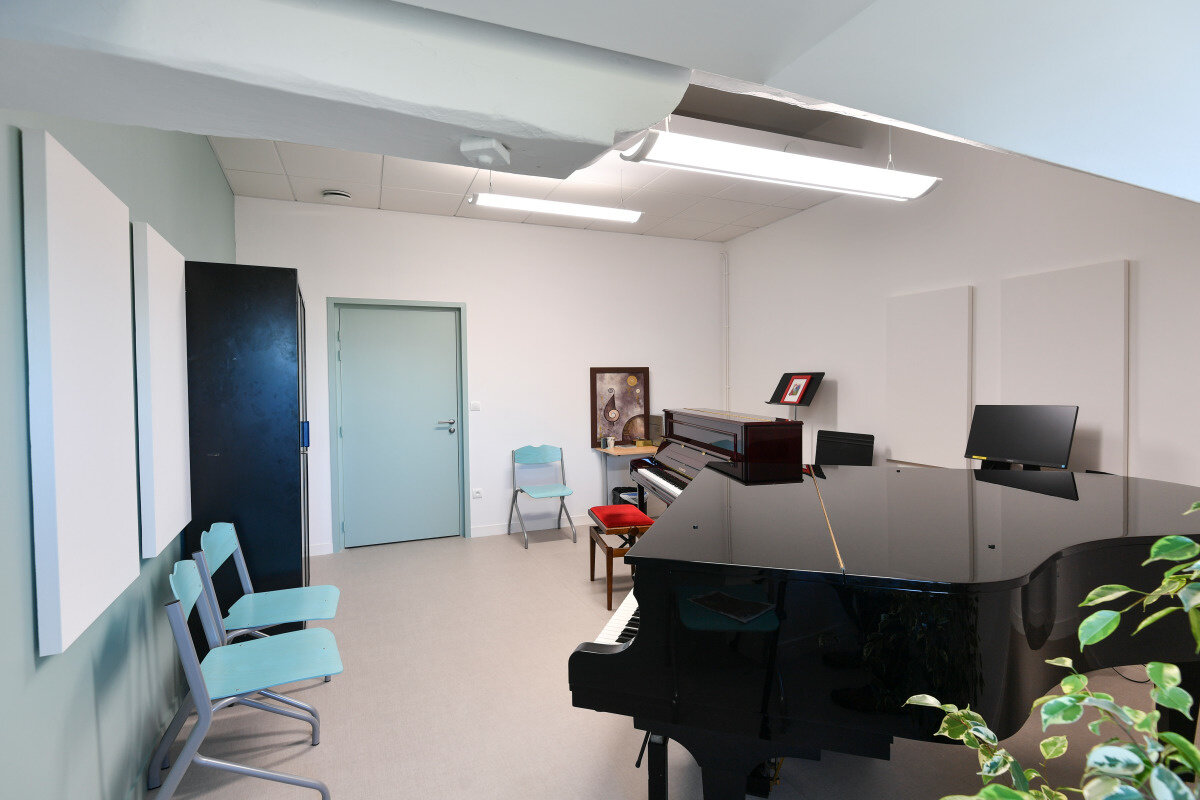 Salle de cours du Conservatoire équipée d'un piano à queue et d'un piano droit, avec panneaux acoustiques