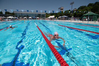 Nageurs dans les couloirs du bassin extérieur en plein soleil, avec le bâtiment de la piscine en fond