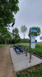 Station VLS Portes du Marais avec vélos bleus alignés sur rack et panneau d'information, le long d'un chemin arboré