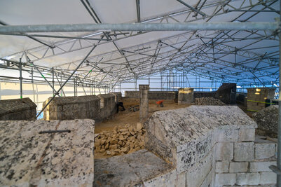 Plateforme sommitale couverte d'une tente de chantier sur échafaudages métalliques, blocs de tuffeau au sol et artisan à l'œuvre