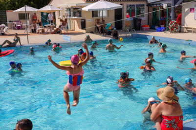 Enfant sautant dans le grand bain de la piscine de Magné, bras levés, entouré de nombreux participants