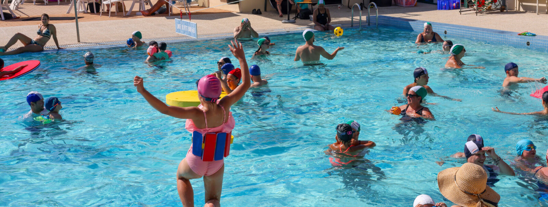 Enfant sautant dans le grand bain de la piscine de Magné, bras levés, entouré de nombreux participants