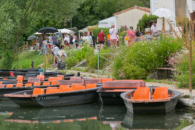 Barques amarrées sur la Sèvre à Coulon, visiteurs déambulant en bord d'eau lors du festival de peinture du Marais poitevin