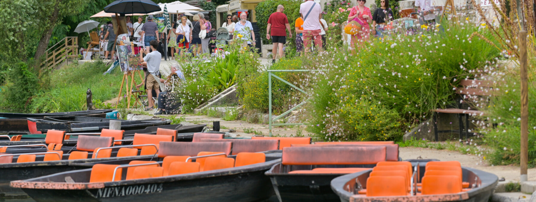Barques amarrées sur la Sèvre à Coulon, visiteurs déambulant en bord d'eau lors du festival de peinture du Marais poitevin