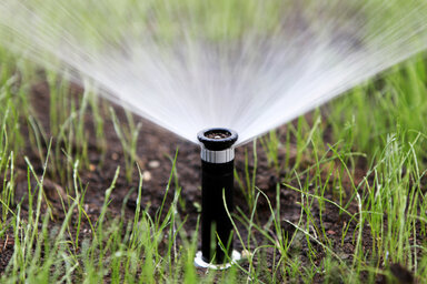 Tête d'arrosage automatique en fonctionnement, diffusant de l'eau en éventail sur une pelouse