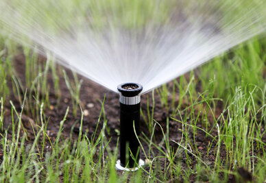 Tête d'arrosage automatique en fonctionnement, diffusant de l'eau en éventail sur une pelouse