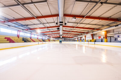 Piste de glace lisse et brillante fraîchement surfacée, tribunes vides et charpente métallique rouge de la patinoire en arrière-plan
