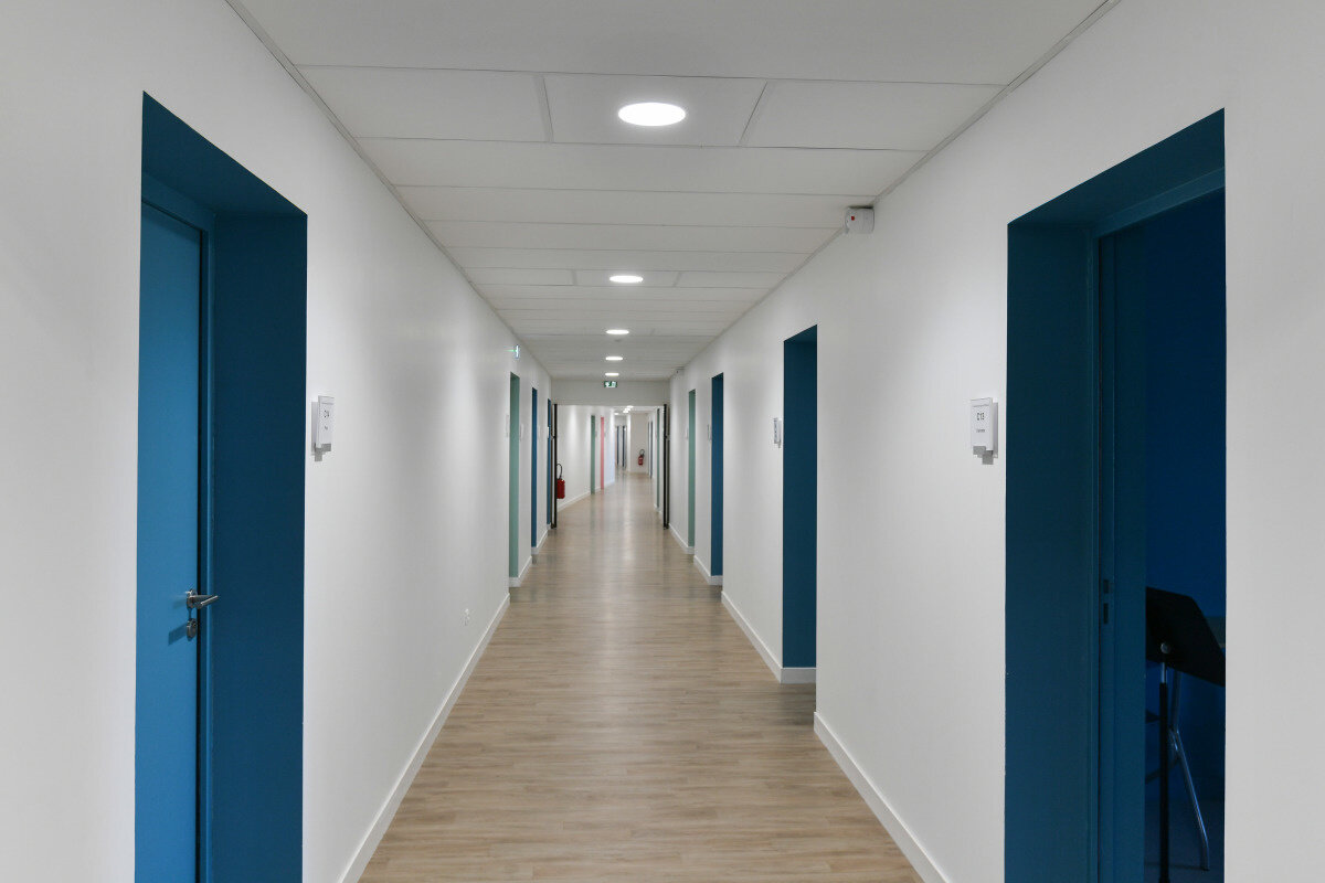 Couloir du Conservatoire avec portes bleues, murs blancs et parquet clair, un pupitre de musique visible dans une salle