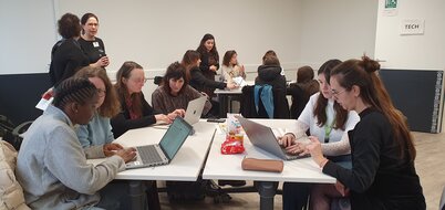 Participantes réunies en petits groupes autour d'ordinateurs portables lors d'un atelier pratique dans une salle estampillée TECH