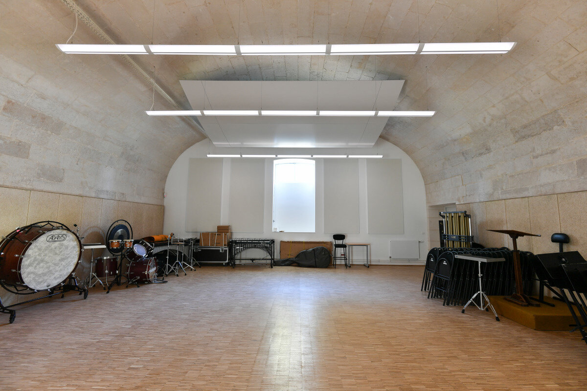 Salle de répétition voûtée du Conservatoire, avec percussions, chaises empilées et parquet en bois